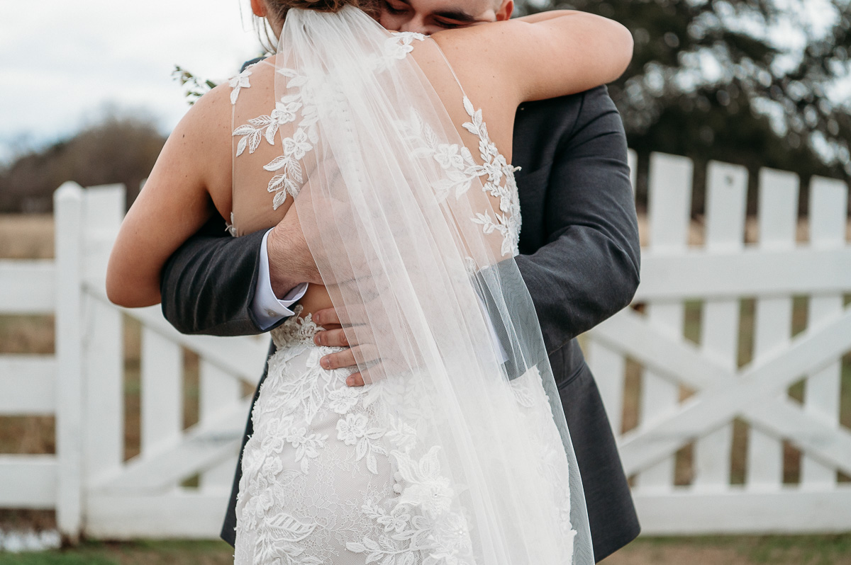 A close up image of a bride and groom embracing on their wedding day with an emphasis on the groom's hands on the bride's back.